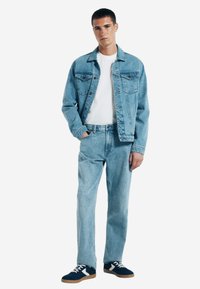 Giacca di denim e jeans in blu chiaro con una t-shirt bianca. Sneakers casual con accenti navy e bianchi. Vestibilità dritta, dettagli di cucitura minimi.