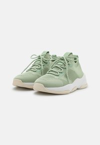 Paire de baskets en maille vert clair avec semelles épaisses blanches et lacets, vue latérale en angle sur fond blanc uni.