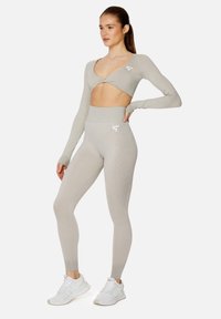 Hellgraues Sportoutfit bestehend aus einem Langarm-Croptop und hochgeschnittenen Leggings mit einem Verlaufstextur. Weißes Logo-Detail auf den Leggings.