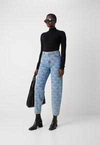 High-waisted blue patterned jeans, black long-sleeve top, black square sunglasses, and a textured black handbag. Black ankle boots complete the look.