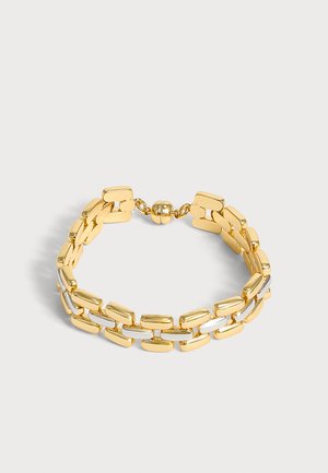 Bracelet rectangulaire en or et argent avec un fermoir arrondi sur un fond gris clair.