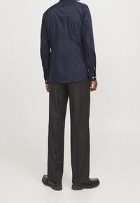 Marinblå långärmad skjorta med rundad nederkant, knappmanschetter och en mjuk textur, ihop med svarta vida byxor och svarta skor.