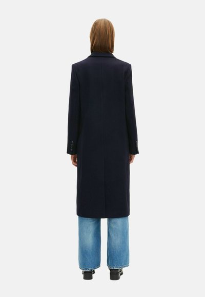 Marineblauwe wollen lange jas met een gekartelde kraag en enkele split, gecombineerd met lichtblauwe wijdvallende jeans en zwarte enkellaarsjes.