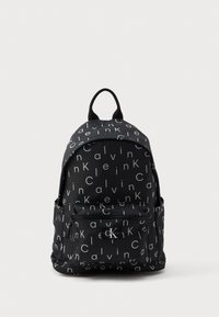 Μαύρο σακίδιο διαθέτει επαναλαμβανόμενο σχέδιο κειμένου με την ένδειξη "Calvin Klein" σε λευκό. Περιλαμβάνει μπροστινή τσέπη με φερμουάρ και μία λαβή στην κορυφή για μεταφορά.