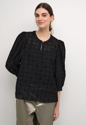 Schwarze bestickte Bluse aus transparenter Fabrik mit strukturiertem Muster, rundem Ausschnitt und puffartigen Ärmeldesign. Vorderer Schlitz mit Knopfakzent.
