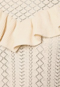 Top de punto color crema con un escote con volantes, fabricado con una mezcla de algodón transpirable, con patrones texturizados de calados y detalles delicados.