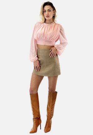 Helles rosa, kurz geschnittenes Blusenshirt mit Puffärmeln, beiger Wildleder-Minirock und knielangen Karamell-Stiefeln mit Stiletto-Absatz.