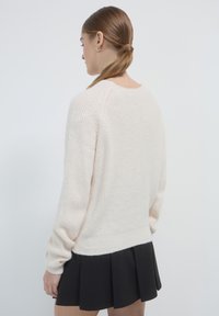 Hellrosaner, gestrickter Pullover mit langen Ärmeln und gerippter Textur, kombiniert mit einem schwarzen, plissierten Rock. Der Pullover hat eine lockere Passform und einen runden Ausschnitt.