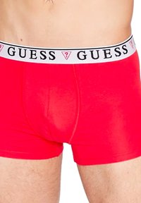 Piros boxer alsónadrág fehér elasztikus derékpánttal, amelyen a "GUESS" logó fekete színben található. Simább, rugalmas anyagból készült.