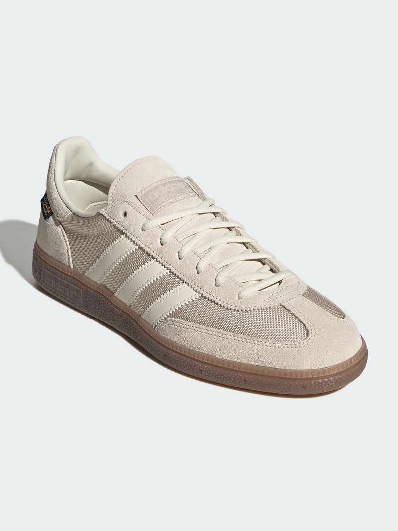 Beige sportskor med överdel i mocka och mesh, med tre vita sidostripes, en texturerad gummisula och en sydd etikett.