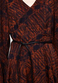 Braun- und dunkelblau gemustertes Kleid mit V-Ausschnitt, langen Ärmeln und einem geschnürten schwarzen Gürtel, der die Taille definiert. Textil mit Struktur.