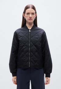 Μαύρο μπουφάν bomber με καπιτονέ ύφασμα, κλείσιμο με φερμουάρ, ριμπ μανσέτες και μικρό λογότυπο στο στήθος. Διαθέτει λεία, γυαλιστερή υφή.