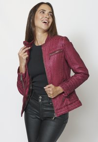 Karmiinpunane kunstnahast jakk tekstuurse viimistlusega, tõmblukuga taskud, ribakujulised õlavarre aktsendid ja siseõmblustega siluett.