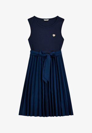Abito navy a costine con design senza maniche, gonna plissettata e cintura coordinata. Presenta un accento a forma di cuore dorato sul corpo.