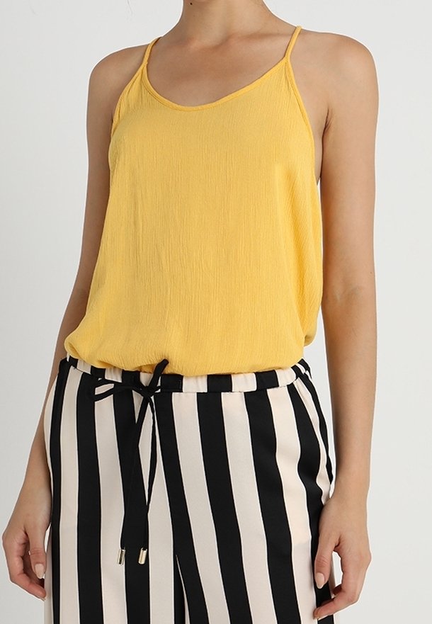 Top sin mangas amarillo con un tejido texturizado, con tirantes finos y un corte relajado, combinado con pantalones de tiro alto a rayas en blanco y negro.