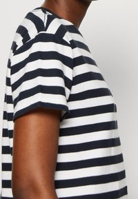 Stribet t-shirt med navy og hvide vandrette striber, korte ærmer, rund halsudskæring og blødt bommateriale. Nærbillede af siden.