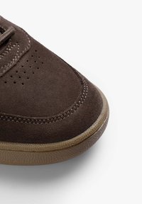 Bruna mockakängor med rund tå, kontrasterande beige gummisula, perforerad detaljering och vita sömmar längs kanterna.