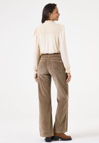 Crème blouse met smock achterkant, gecombineerd met lichtbruine corduroy broek met zakken en een recht model. Bruine enkellaarsjes.