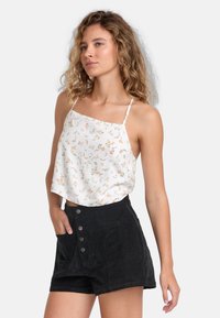 Blomstrete, ærmeløs hvid crop top med spaghettistropper, parret med højtaljede, sorte kordfløjlsshorts med knapdetaljer og lommer.