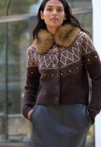 Brun stickad cardigan med geometriska mönster, krage av fuskpäls och knappdetalj; kombinerad med en slät svart läderkjol.