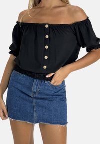 Schwarzes schulterfreies Oberteil mit Puffärmeln, versehen mit sechs Holzknöpfen und einem gerafften Bund, kombiniert mit einem hellblauen Jeans-Minirock.