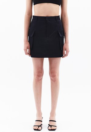 Donkerblauwe mini rok van gladde stof, met twee voorkant cargozakken, een getailleerde taille en een rechte silhoeet. Gestyled met zwarte spaarzaam hakken.