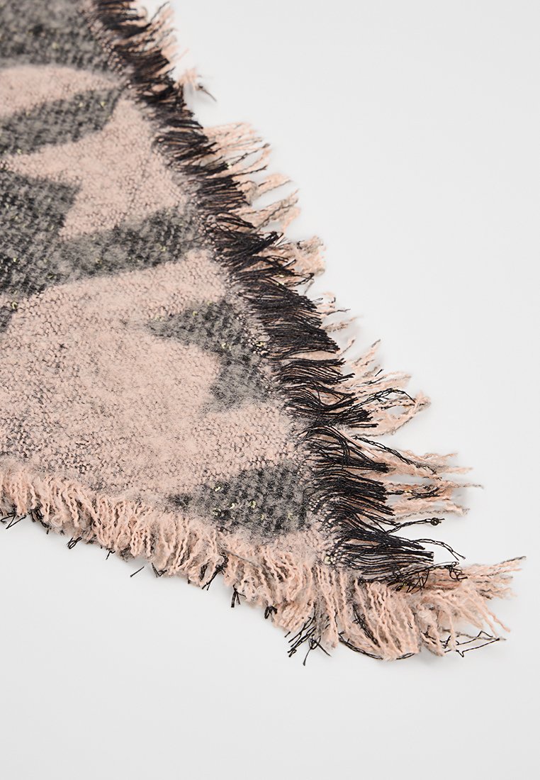 Esquina de una tela suave de color rosa y gris con un patrón, con bordes deshilachados y un fleco con borlas negras y rosas sobre un fondo blanco.