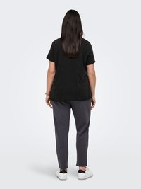 Black short-sleeve t-shirt with a loose fit, paired with gray tapered pants. Model is facing away, wearing white sneakers with black accents.