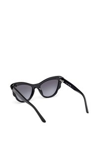 Gafas de sol de cat-eye negras con lentes oscuros en degradado. La montura presenta un acabado brillante y acentos ligeramente elevados en el borde superior.
