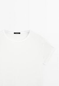 Weißes Baumwoll-T-Shirt mit Rundhalsausschnitt und kurzen Ärmeln. Verfügt über ein kleines schwarzes Etikett am Hals. Glatte Textur, minimalistisches Design.