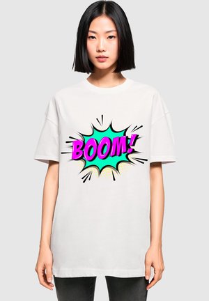Biała, oversize'owa koszulka z kolorową grafiką w stylu komiksowym z napisem "BOOM!" w różowym i turkusowym kolorze, podkreśloną czarnymi konturami i kropkami.