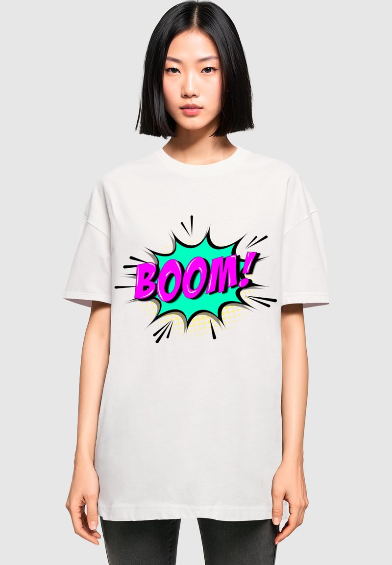 Balta didelis t-shirt'as su spalvinga komiksų stiliaus grafika, kurioje žodis "BOOM!" pavaizduotas rožine ir mėtų spalvomis, supaprastintas juodais kontūrais ir taškeliais.