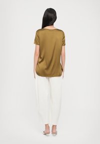 T-shirt in raso verde oliva con maniche corte, caratterizzato da un collettino a girocollo e un orlo leggermente curvato, abbinato a pantaloni bianchi a gamba larga.
