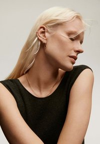 La joyería de oro realza a una modelo que lleva una blusa sin mangas de color oscuro. Los pendientes presentan una mezcla de formas y texturas, mejorando el aspecto general.