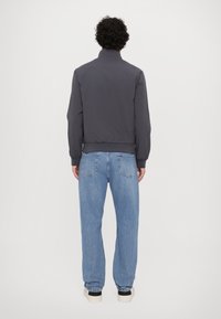 Mørk grå bomberjakke med høy krage, ribbestrikkede mansjetter og elastisk midje, sammen med lyseblå rett-fasong jeans. Uformelt fottøy synlig.