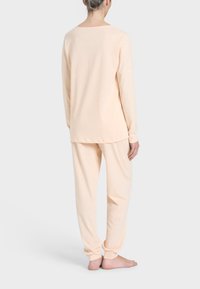 Set di abbigliamento da lounge in morbido pesca, composto da top a maniche lunghe e pantaloni. Tessuto leggero e liscio con una vestibilità comoda e polsini a coste alle caviglie.