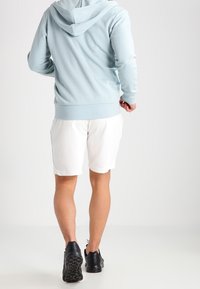 Sweat à capuche bleu clair avec capuche, poignets et ourlet côtelés. Associé à un short blanc et des baskets noires, vu de dos.