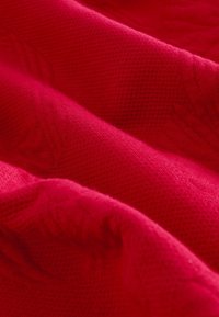 Tissu rouge texturé avec un motif tricoté doux. Le matériau présente un design côtelé subtil, créant de la profondeur et un intérêt visuel.