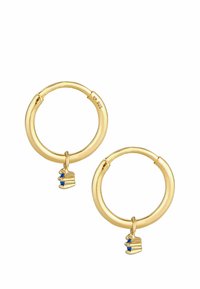 Pendientes de aro en tono dorado con un acabado suave. El charm adjunto se asemeja a un pastel, embellecido con dos piedras azules. Forma redonda, textura pulida.