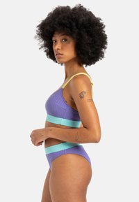 Lilla ribbestrikket badedraktsett med bandeau-topp med lys blå detaljer og matchende underdel. Justerbare gule stropper og minimalistisk design.