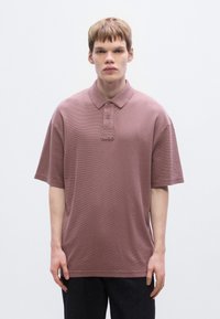 Πόλο μπλουζάκι με κοντά μανίκια σε απαλό βουργουνδί χρώμα, υφασμένο ύφασμα. Διαθέτει γιακά, πλάκα με δύο κουμπιά και διακριτική κεντητή λογότυπο στο στήθος.