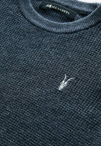Maglione testurizzato blu scuro con scollo a girocollo a coste e un piccolo logo bianco ricamato sul davanti, che mostra un motivo intrecciato.