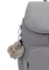 Sac à dos en tissu gris avec une poche avant et une fermeture éclair, featuring un porte-clés en forme de singe en peluche beige attaché sur le côté.