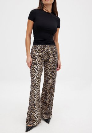 Pantalones acampanados de estampado de leopardo en beige y negro, combinados con una blusa ajustada negra de manga corta y zapatos negros de punta. Textura suave.