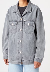 Grå denim jacka med knappstängning framtill, två bröstfickor med dekorativ sömnad och en avslappnad passform.