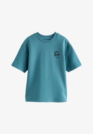 Teal puuvillapaita, jossa on lyhyet hihat ja pyöreä kaula-aukko. Huomattava musta pääkallo, jolla on kuulokkeet vasemmassa rintataskussa.