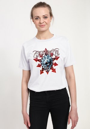 T-shirt en coton blanc avec un graphique coloré d'une tête de mort entourée de flèches rouges et le texte « Éclats du Mal » au-dessus. Manches courtes.