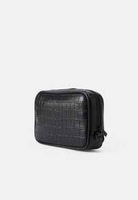 Črna torbica iz usnja s kroko embosiranjem, pravokotne oblike, z zadrgo in gladko površino. Ima diskretne kovinske dodatke.