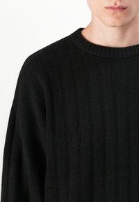 Sort ribbet strikket sweater med rund halsudskæring, der har et struktureret mønster og en afslappet pasform, som fremviser en blød finish.