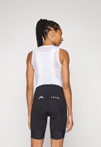 Melni velo šorti ar ieliktni sēdeklim un balta, bez piedurknēm, acu tīkla krekls, kas izceļas ar diskrētu logotipu un pieguļošu siluetu.